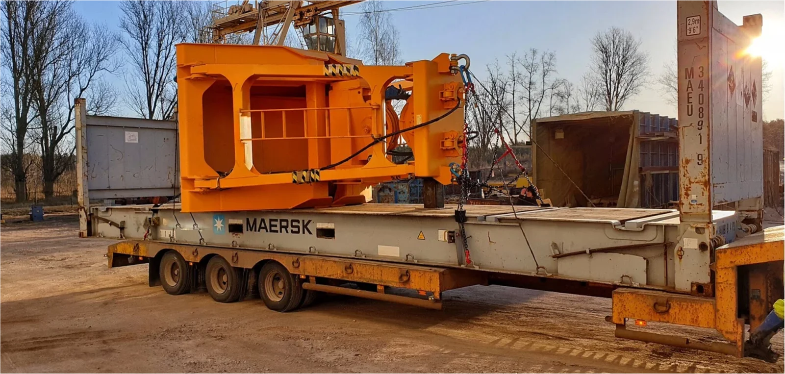 A large yellow component of crane equipment, classified as oversized cargo, securely fastened onto a red flatbed trailer pulled by a blue truck for its road transport phase from Latvia to a European port, en route to Guinea.